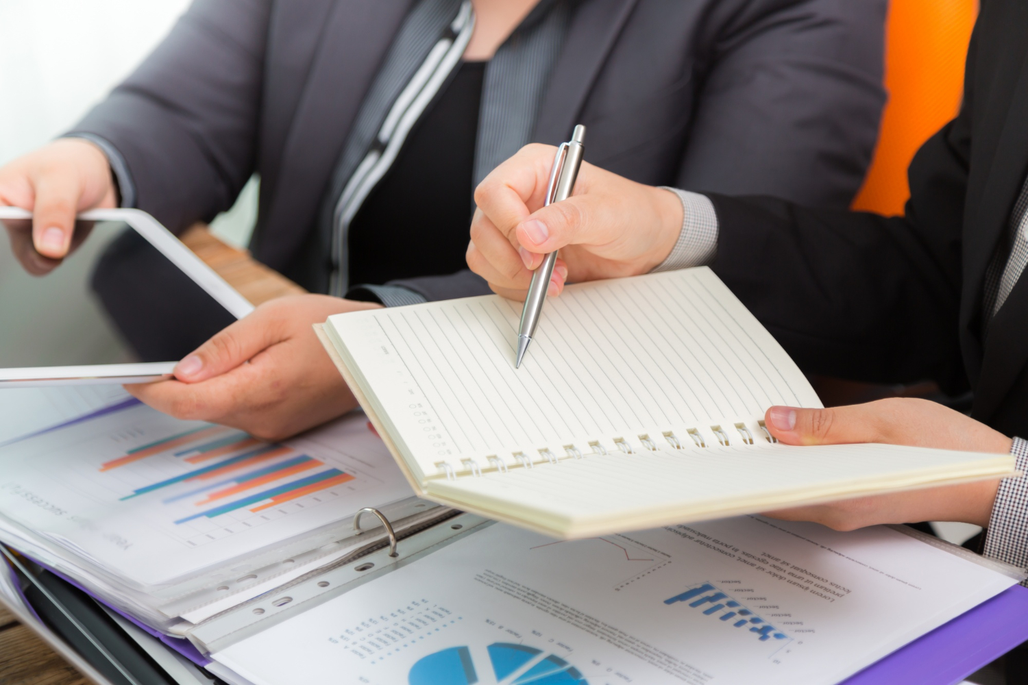 Two procurement reviewers examining printed audit charts and a tablet during a documentation review